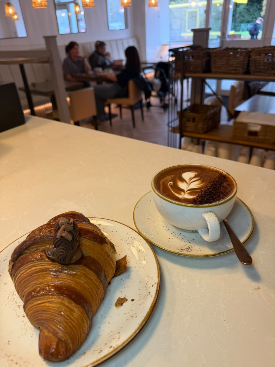 A chocolate croissant and a mocha with latte art on the counter inside Thrive, with guests in the booths behind